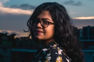Profile portrait of a young woman with glasses outdoors during sunset.